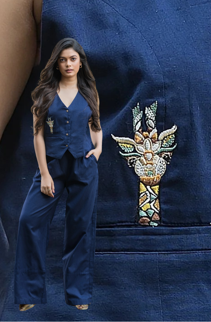 Woman in a blue outfit standing next to a dark blue fabric with an embroidered design.